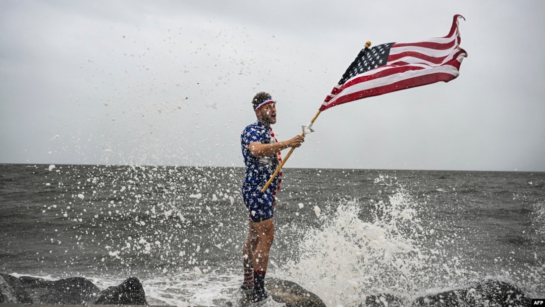 Youtuber Mark Peyton holds a US flag as he poses for his brother Matt Peyton on the shoreline ahead of the arrival of Hurricane Helene in Alligator Point, Florida, on Sept. 26, 2024. 