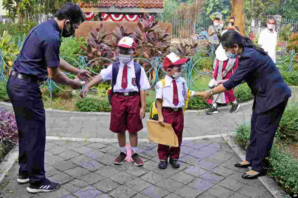 Staff members check body temperatures of students on the first day of school reopening in Jakarta, Indonesia.