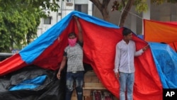 An Indian fruit vendor wearing face mask to protect from the coronavirus uses a plastic sheet to cover from rain in Hyderabad, India, July 23, 2020.