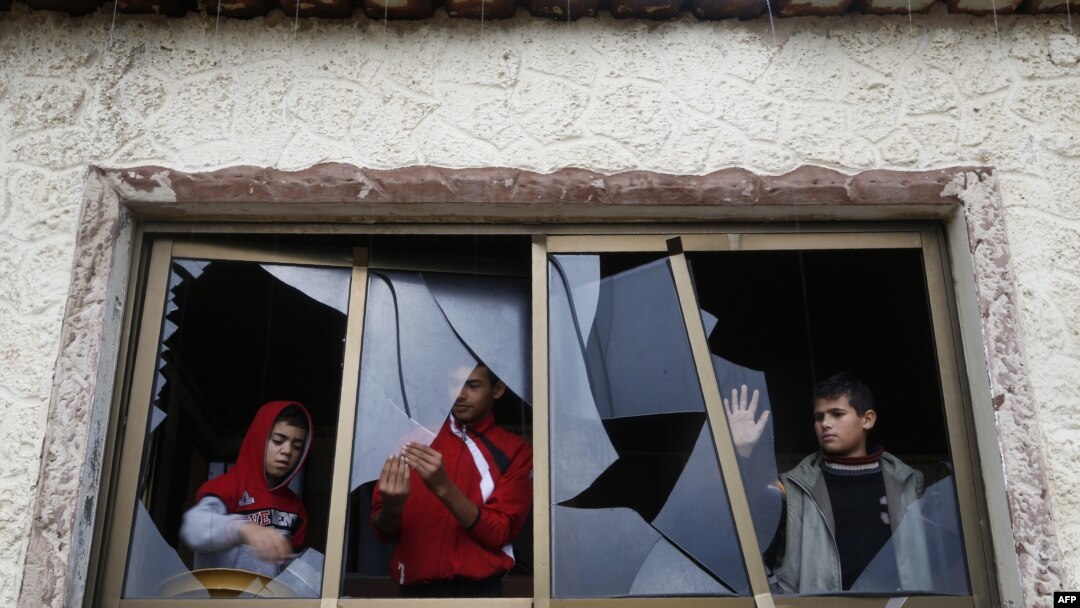 Palestinian boys pull shards of glass from a broken window at their home near the site of Israeli overnight attacks in Gaza City, Dec. 8, 2019.