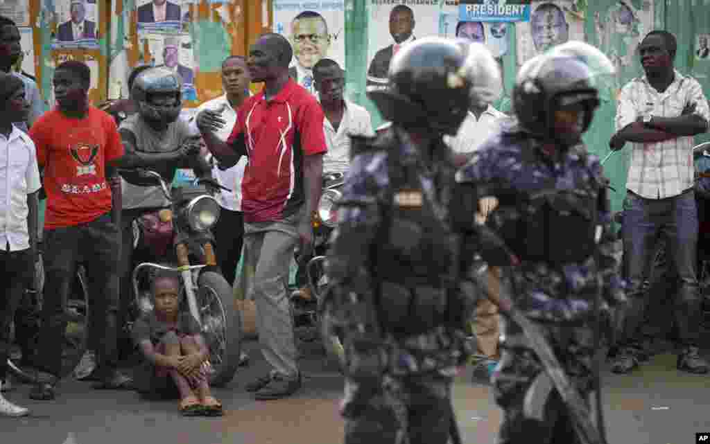 Ugandan riot police stand close to dejected opposition supporters to prevent them from demonstrating, shortly after the election result was announced, in downtown Kampala, Uganda, Feb. 20, 2016.