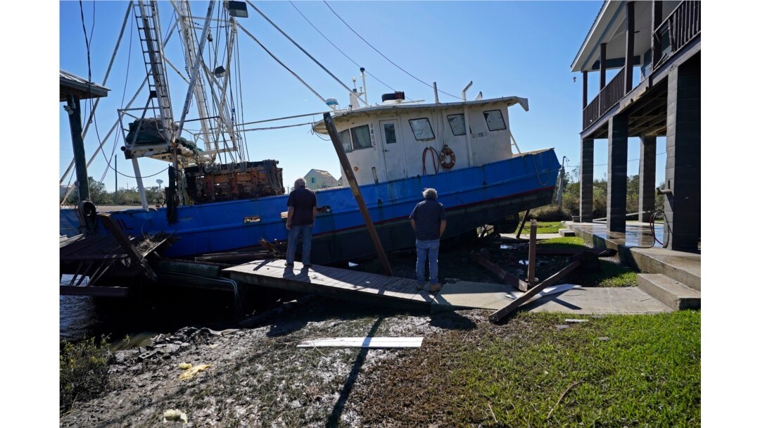 Boat owner Ricky Mitchell, left, surveys damage to his boat that Hurricane Zeta washed up against a home in Lakeshore, Miss., Oct. 29, 2020.