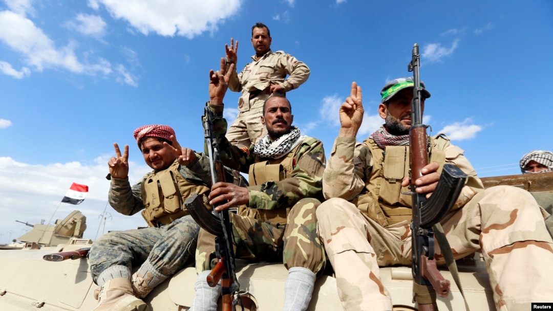 Members of the Iraqi security forces and Shi'ite fighters sitting on a military vehicle gesture in the town of Hamrin, in the Salahuddin province, March 3, 2015.