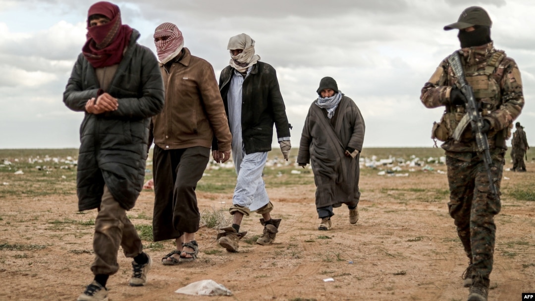Men suspected of being an Islamic State (IS) group's fighter walk next to a member of the Kurdish-led Syrian Democratic Forces (SDF) as they wait to be searched after leaving the IS group's last holdout of Baghouz, Syria, Feb. 27, 2019.