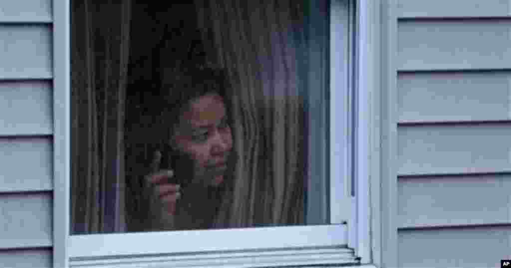 A woman looks out a window at her home as police start to search an apartment building while looking for a suspect in the Boston Marathon bombings in Watertown, April 19, 2013.