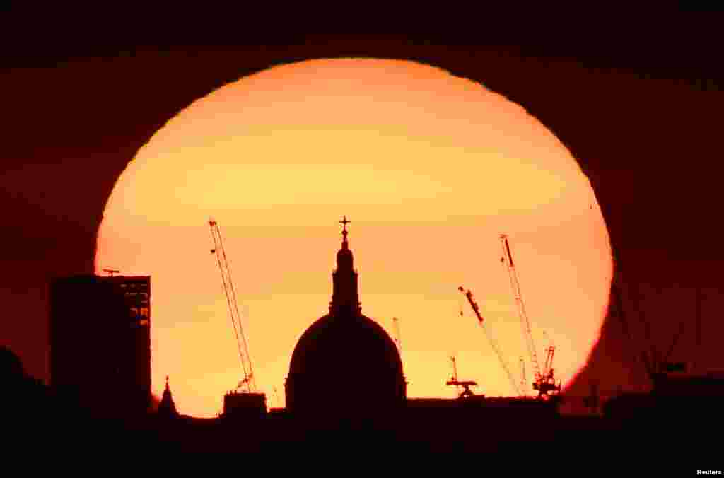 The dome of St. Paul's Cathedral and construction cranes are silhouetted by the rising sun at dawn in London.