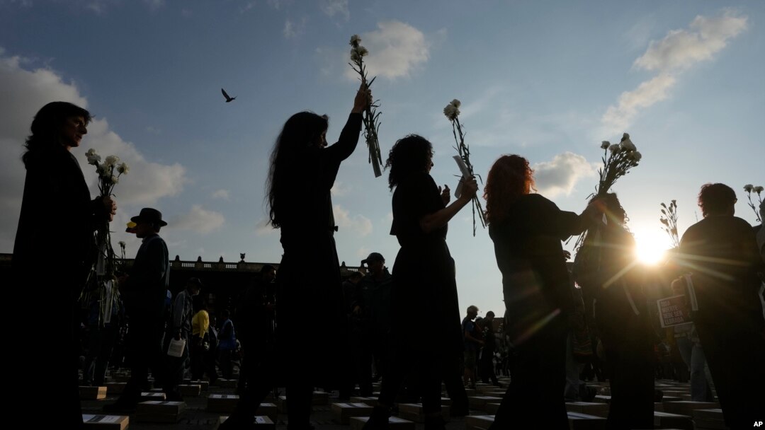 ARCHIVO - Las mujeres sostienen flores y caminan entre cajas que representan ataúdes simbólicos mientras recuerdan a exguerrilleros y líderes sociales que han sido asesinados desde la firma de un acuerdo de paz en 2016, en Bogotá, Colombia, el martes 20 de febrero de 2024.
