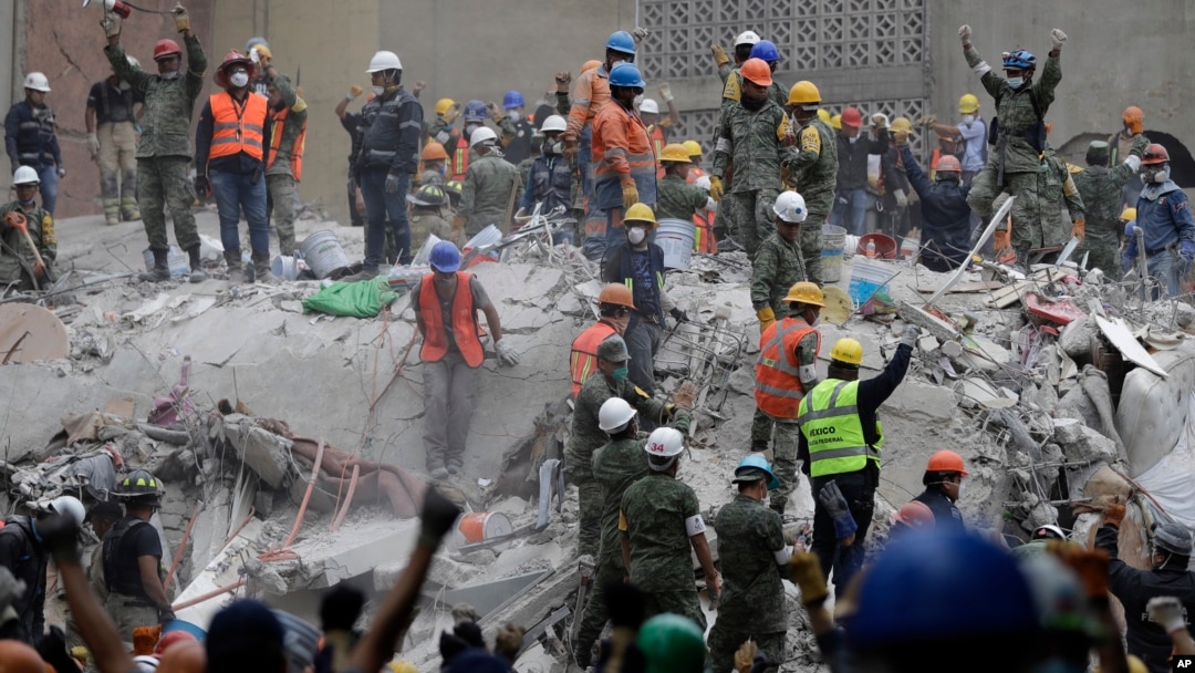 Rescue workers, some holding their arms up as a sign to maintain silence, search for survivors at an apartment building at Amsterdam and Laredo streets that collapsed during an earthquake in the Condesa neighborhood of Mexico City, Mexico, Sept. 21, 2017.