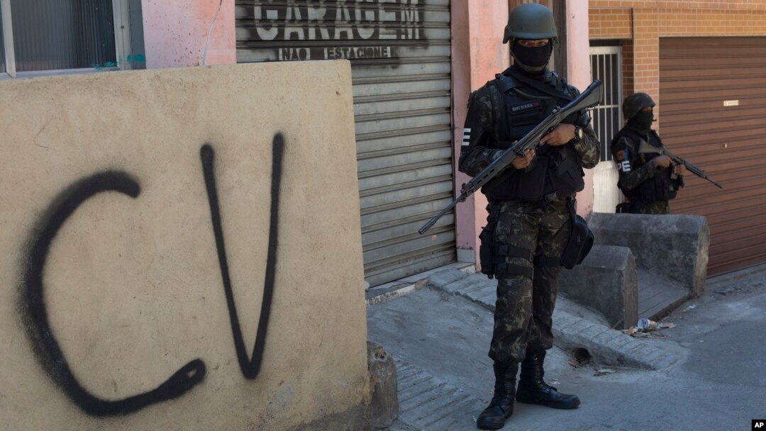 FILE - A soldier stands guard next to a wall tagged with the acronym "CV" identifying the criminal organization "Comando Vermelho" or Red Command, during an operation at the Rocinha slum, in Rio de Janeiro, Brazil, Oct. 10, 2017. 