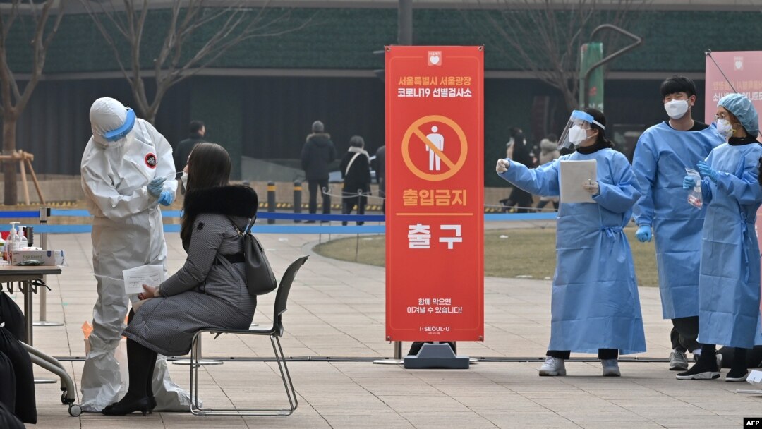 A medical staff member (L) wearing protective gear takes a swab from a visitor to test for the COVID-19 coronavirus at a temporary testing station outside the City Hall in Seoul on December 23, 2020, as South Korea banned gatherings of more than four peop