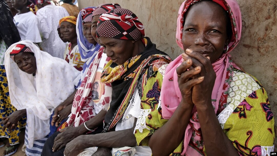 FILE - Women wait outside the workroom of the Multi-functional Platform for Poverty Alleviation in the village of Poa near Ougadougou in Burkina Faso.