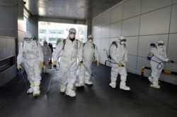This handout picture taken Feb. 19, 2020, by Daegu Metropolitan City Namgu shows workers in protective suits spraying disinfectant in front of the Daegu branch of the Shincheonji Church of Jesus in the southeastern city of Daegu, South Korea.