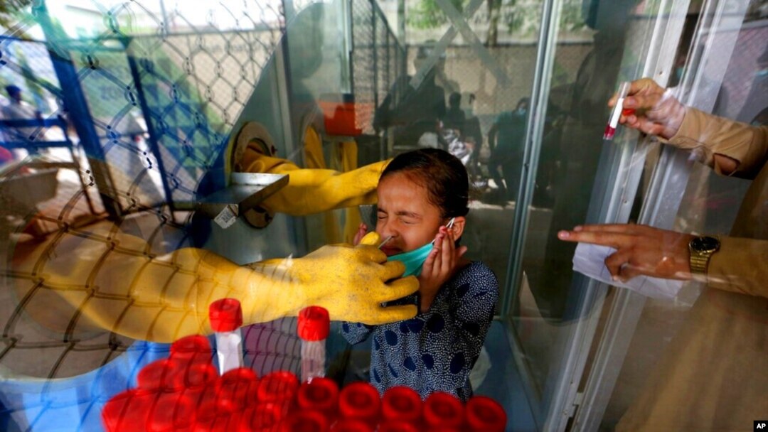 FILE - A girl reacts while having a nasal swab sample taken by a health worker at a COVID-19 testing facility in a hospital in Karachi, Pakistan, March 18, 2021. 