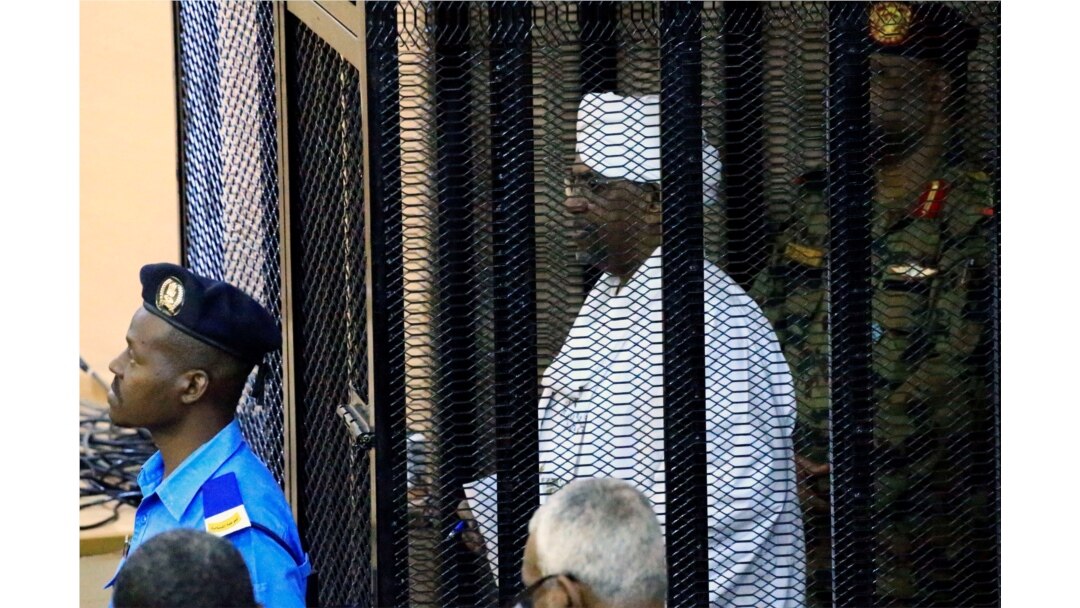 FILE - Sudan's former president Omar Hassan al-Bashir stands guarded inside a cage at the courthouse where he is facing corruption charges, in Khartoum, Sudan, Aug. 19, 2019.